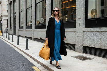 Woman in black coat and white dress holding a yellow bag on a city street.