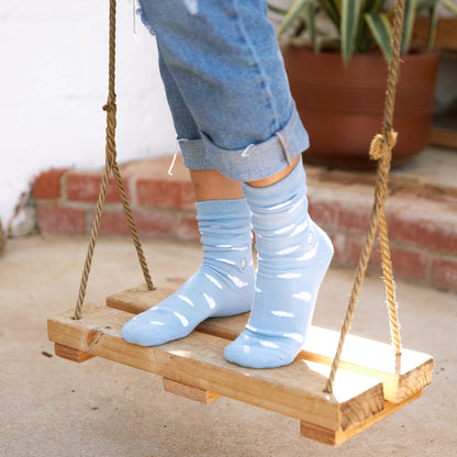 Person wearing light blue socks on a wooden swing with a plant in the background.