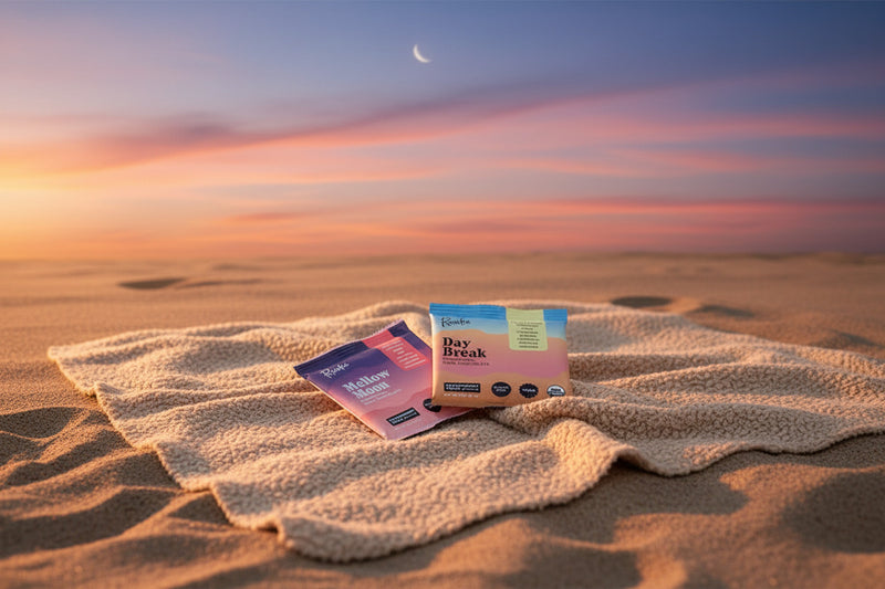 Two packages of Raaka chocolate, 'Mellow Moon' and 'Day Break', on a blanket in the sand