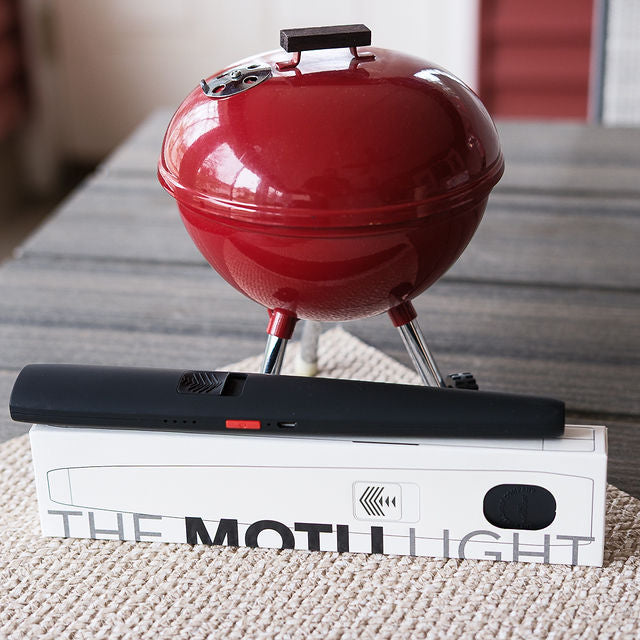 Red portable grill on a stand with a 'The Motley' product box in the foreground.