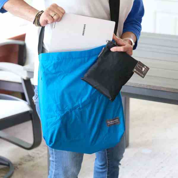 Person holding a blue bag with a black drawstring pouch, wearing a white shirt and blue jeans.