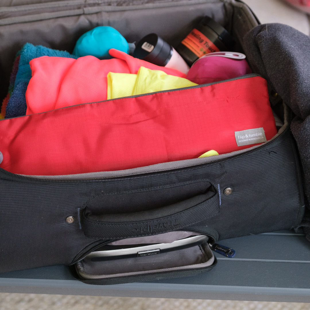 Open suitcase with colorful clothes and a red folded backpack inside