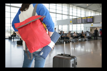 Person with a red backpack and a blue folded one in her hands. She is at the airport.