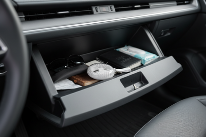 Car console with open storage compartment containing items like sunglasses and a phone.