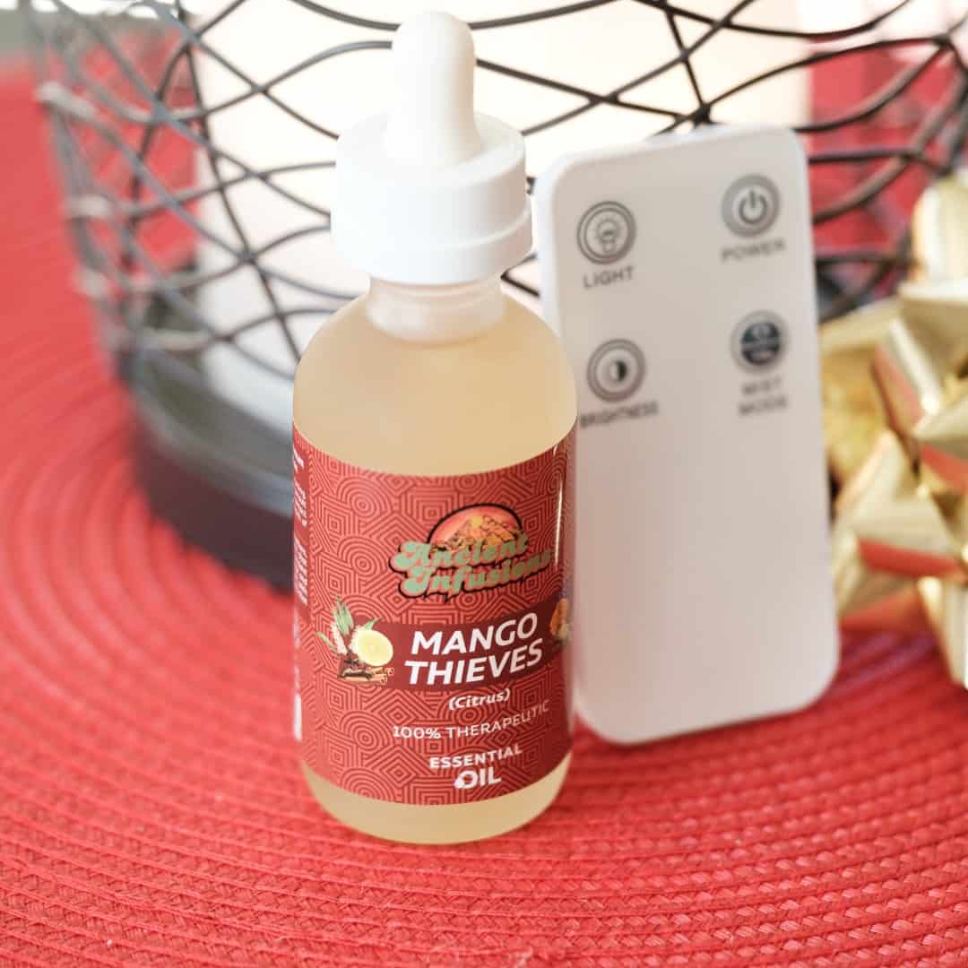 Bottle of Mango Thieves essential oil with a remote control and diffuser on a red surface