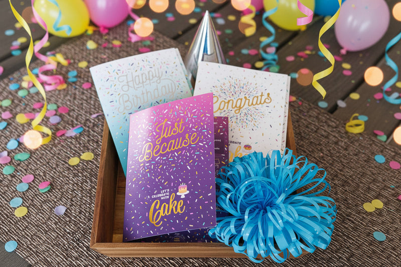 Three greeting cards with celebratory messages in a wooden box on a textured surface.