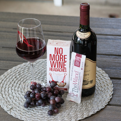 Bottle of red wine, glass with wine, grapes, and 'No More Wine Headaches' product on a textured surface.
