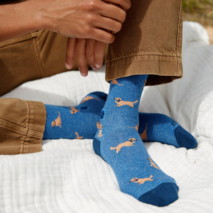 Person wearing blue socks with dog pattern on a white blanket