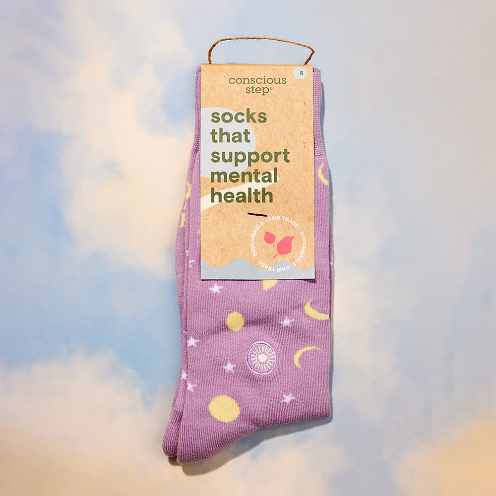 Purple socks with celestial design and 'conscious step' packaging on a soft, blurred background