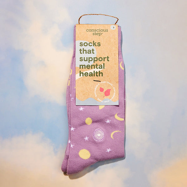Purple socks with celestial design and 'conscious step' packaging on a soft, blurred background